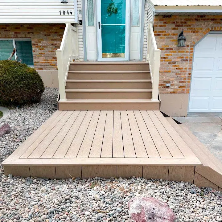 A modern light gray composite porch area installed under an existing roof overhang, secured with sleek black metal railings.