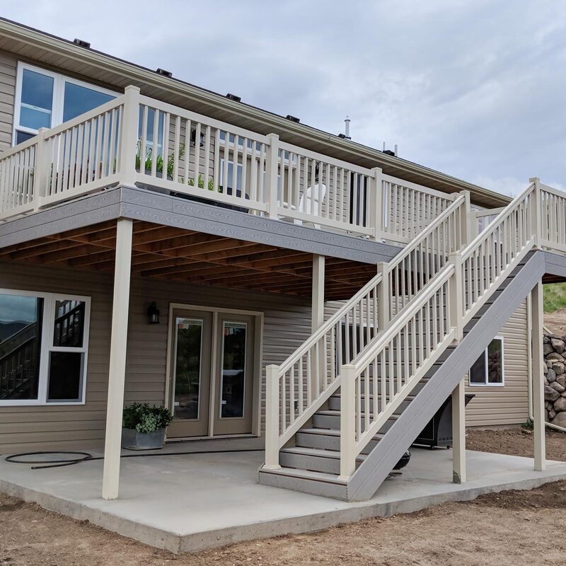 Elevate your outdoor living with this expansive two-story deck, designed for seamless access and modern style. The upper level features durable composite decking and classic white vinyl railings, perfect for entertaining or relaxing with views. A sturdy staircase, with matching railings, connects the levels and leads down to a practical concrete patio, expanding your functional outdoor space. This low-maintenance design offers a sophisticated look that complements your home.