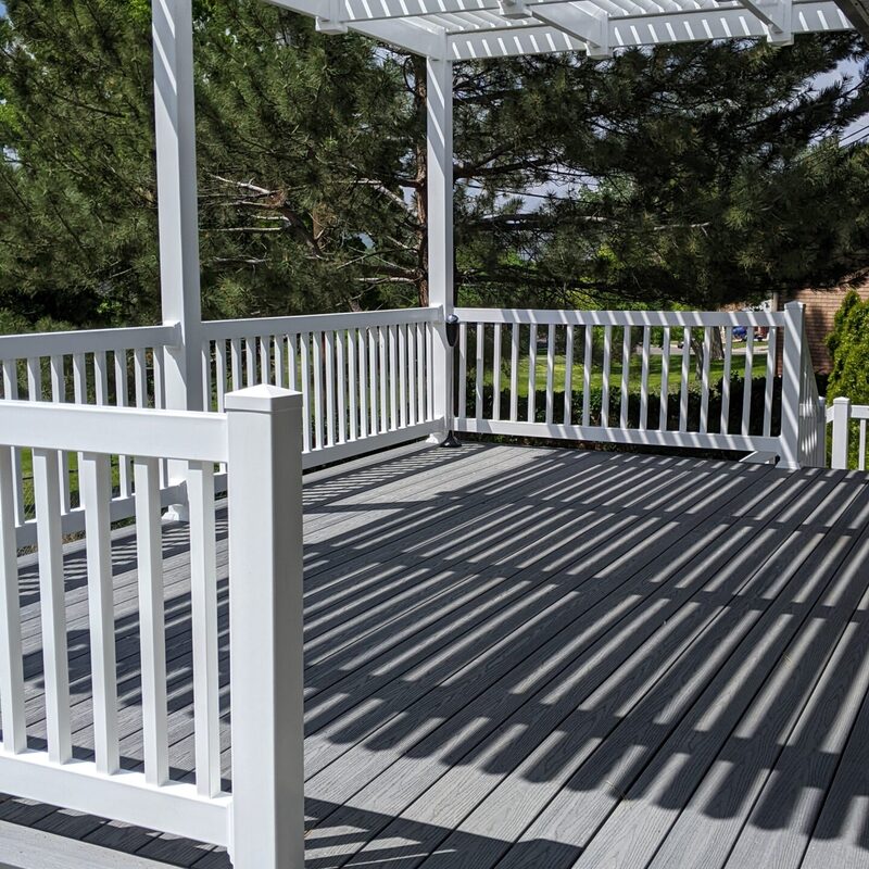 Extend your upper-level living space with this cozy raised composite deck by DeckPro LLC, designed for tranquility and function. We installed low-maintenance composite decking in a warm brown tone and a matching perimeter railing system. Furnished with a comfortable dark Adirondack chair, it's the perfect retreat to take in the serene views of the surrounding pine trees and rustic outdoor setting.