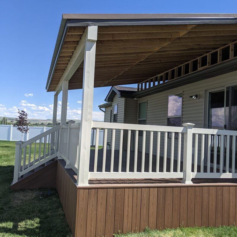Extend your multi-level outdoor living with this dramatic custom raised deck transformation by DeckPro LLC. Pictured bordering natural vegetation on a beautiful day, this sophisticated structure features grey and brown composite planks and safe and sophisticated black vertical perimeter railings that border defined zones. The sturdy retreat is accessible via comprehensive stairs leading down to a lower set of connecting massive wide stairs bordering a dirt trail, defining a tranquillity sanctuary perfect for relaxation or large-scale entertaining under prominent covered upper areas. Direct access via existing sliding glass doors and multiple upper-level entry points ensures effortless flow. Grading work is met by a beautiful rock garden featuring various bushes and large natural boulder rocks on a gravel bed. Integrated features include recessed ceiling lights in covered areas and hidden enclosed storage with doors.