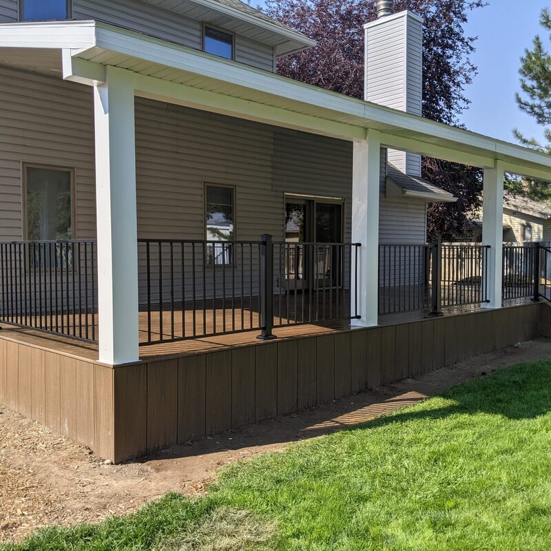 Expand your upper-level living space with this cozy raised fir balcony deck by DeckPro LLC, designed for tranquility and function. This sturdy and stylish retreat uses extensive natural wood decking planks and a full perimeter railing system to create a safe, open retreat. Pictured on a sunny day with distinctive railing shadows, the build overlooks a natural dirt road, expansive pine trees, and a distant basketball hoop, creating a tranquil mountain retreat perfect for taking in scenic woodland views.