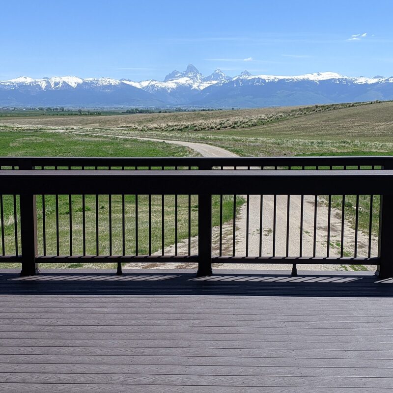 Elevate your outdoor living and entertaining experience with The Teton Vista, a signature custom composite deck by DeckPro LLC. This project features premium, grooved low-maintenance composite decking boards with a rich, multi-tonal grey and brown wood-grain texture. The defining feature is the seamlessly integrated, large railing-mounted serving counter, or drink rail, designed with matching composite materials.