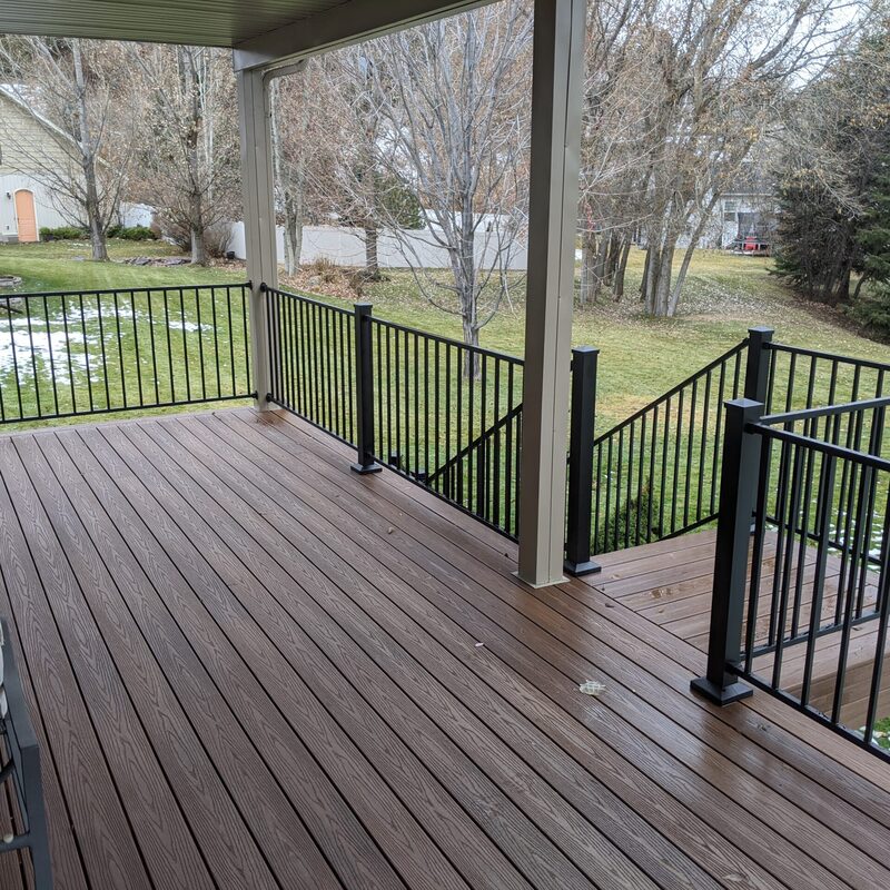 Elevate your outdoor living with the signature Apex Custom Elevated Composite Deck and Safe Access Staircase by DeckPro LLC. This massive elevated (raised) covered deck platform, custom-built, features premium, multi-tonal low-maintenance composite decking boards with a rich wood-grain texture, providing a durable and sophisticated surface. The entire platform is safely enclosed by a modern black metal picket railing system with square posts and decorative pyramid caps, ensuring safety without compromised views.