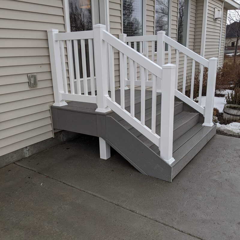 Enhance your home’s main entrance with this custom-designed, elevated composite entry landing and step system by DeckPro LLC. This project features premium, low-maintenance grey composite decking planks on both the upper landing surface and matching stair treads. For a clean, modern look and unmatched safety, we installed a durable white vertical picket railing system with decorative posts and matching pyramid caps.