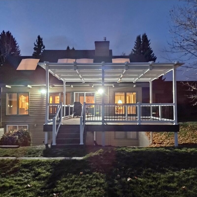 Extend your multi-level outdoor living with this massive multi-zone composite raised deck transformation by DeckPro LLC. Pictured on a beautiful partly cloudy day, this sophisticated structure features expansive gray and brown composite planks paired with sleek black vertical perimeter railings. This sturdy retreat transitions via extensive massive wide staircases with contrasting risers to a stamped concrete lower level and a beautifully landscaped rock garden featuring natural boulder rocks on a gravel bed. Direct access via multiple conversation areas and comprehensive stairs allow for effortless entertaining, while integrated recessed ceiling lighting in the covered upper area ensures evening use. Defining functional zones perfect for both relaxation and large-scale entertaining, this unique tranquilidad sanctuary maximizes spectacular multi-directional natural views. Pictured diptych transformation reveals direct access via sliding glass doors on upper levels to covered sections.