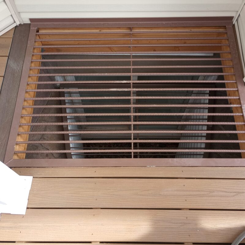 Expand your outdoor living space with this cozy raised deck by DeckPro LLC. We installed high-quality, low-maintenance composite decking in a warm brown tone and paired it with safe and sophisticated dark vertical perimeter railings, creating a sturdy retreat perfect for relaxation. Pictured on a beautiful sunny day with clear skies and distinct shadows cast across the deck boards, this functional build transitions through a massive and inviting set of stairs leading to a stamped concrete patio, creating defined sun and shade areas and optimizing views of the vast backyard. Direct access is available via a sliding glass door.