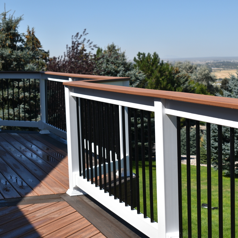 This beautiful residential deck features a custom two-tone railing system installed by DeckPro LLC. It combines classic white vinyl posts with modern black metal balusters and is topped with a flat, brown composite "cocktail rail" that perfectly matches the deck surface. This functional design provides a safe, elegant border to rest a drink on while preserving the sweeping scenic views of the property.
