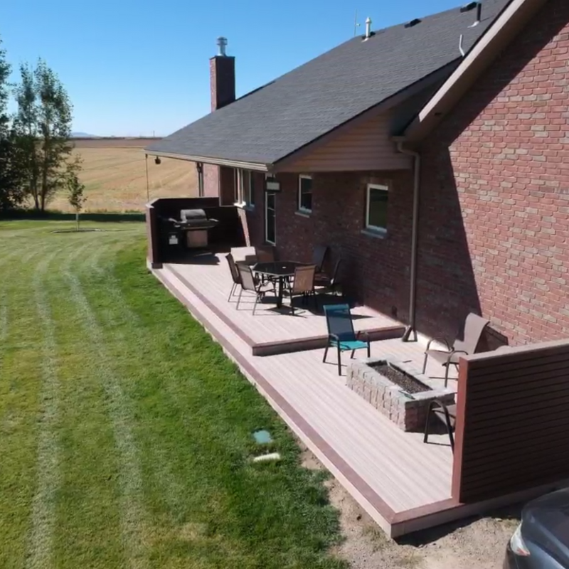 Transform your outdoor living space with a custom ground-level composite deck from DeckPro LLC. This expansive project features light brown composite decking that spans the length of the home, a built-in fire pit for cozy gatherings, and a stylish dark brown privacy wall to create a secluded retreat. It's the perfect blend of function and modern design.