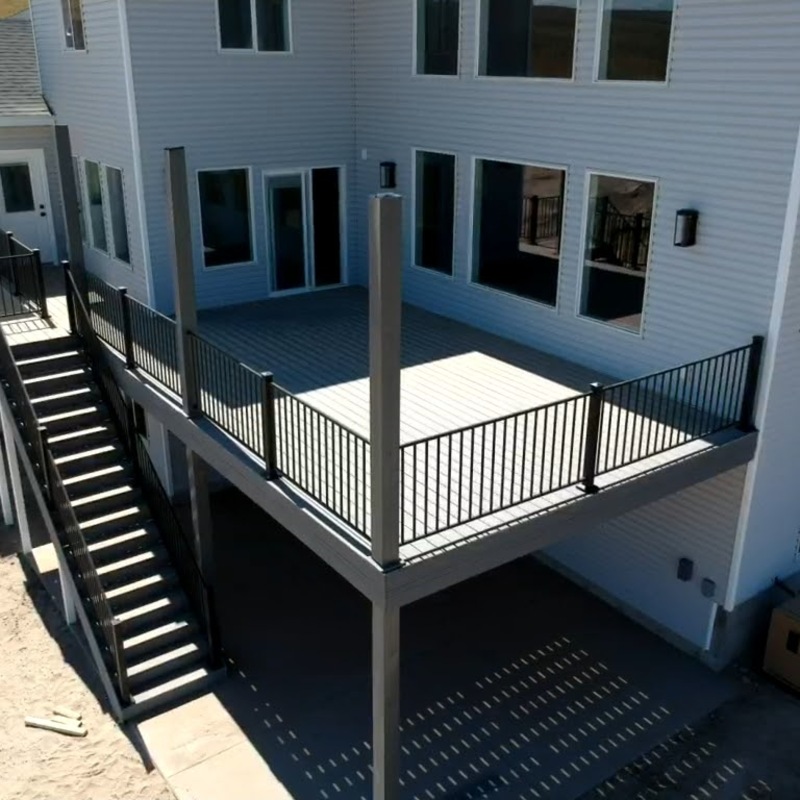 Expand your outdoor living possibilities with this extensive multi-level deck project by DeckPro LLC. We installed high-quality, low-maintenance composite decking in a modern grey tone and paired it with sophisticated black metal perimeter railings that perfectly complement the house exterior. This custom raised structure transitions seamlessly through the massive staircase to a concrete lower level, providing dual living zones perfect for sun or shade. The sturdy design features prominent support posts and offers the ideal retreat for enjoying wide-open natural views, creating a unique and functional backyard sanctuary.