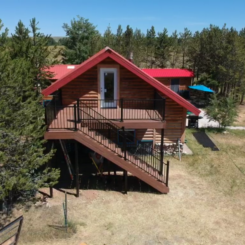 Designed to blend seamlessly with its rustic surroundings, this custom composite deck by DeckPro LLC is the perfect addition to this Idaho log cabin. The project features durable decking, sleek black metal railing, and a staircase for easy backyard access.