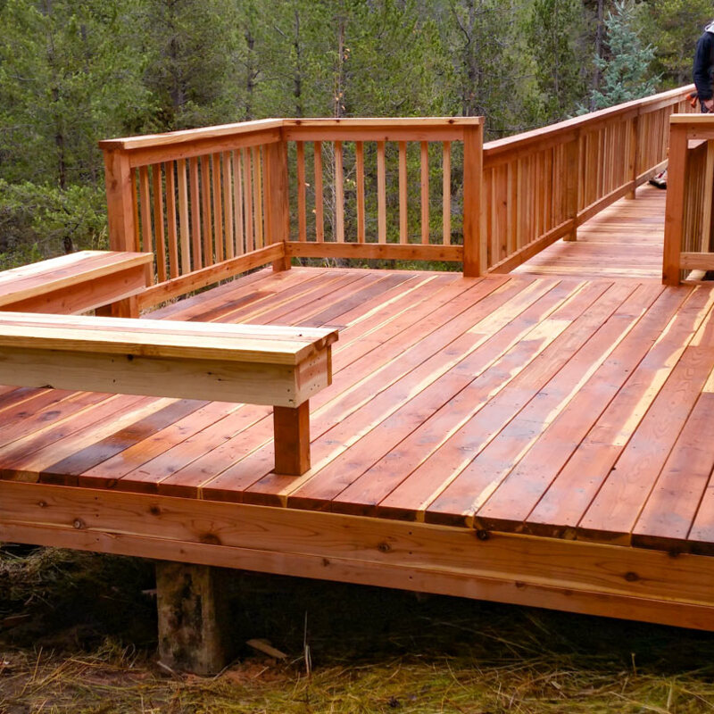 Experience the timeless beauty of natural wood with this custom raised deck by DeckPro LLC. Designed to blend seamlessly into the wooded surroundings, this project features rich wood tones, a sturdy built-in bench for seating, and a convenient long walkway ramp for easy access.