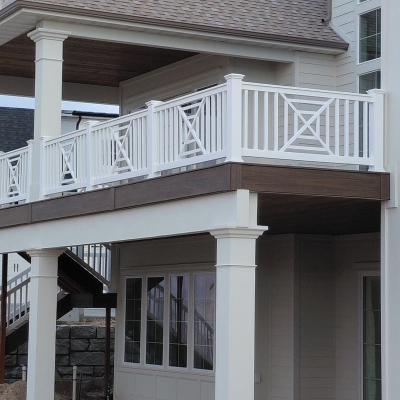 An exterior view of a multi-level deck featuring a custom white vinyl railing installation by DeckPro LLC in Idaho Falls, ID. The project highlights a sophisticated "X" pattern design on a raised balcony and matching staircase.